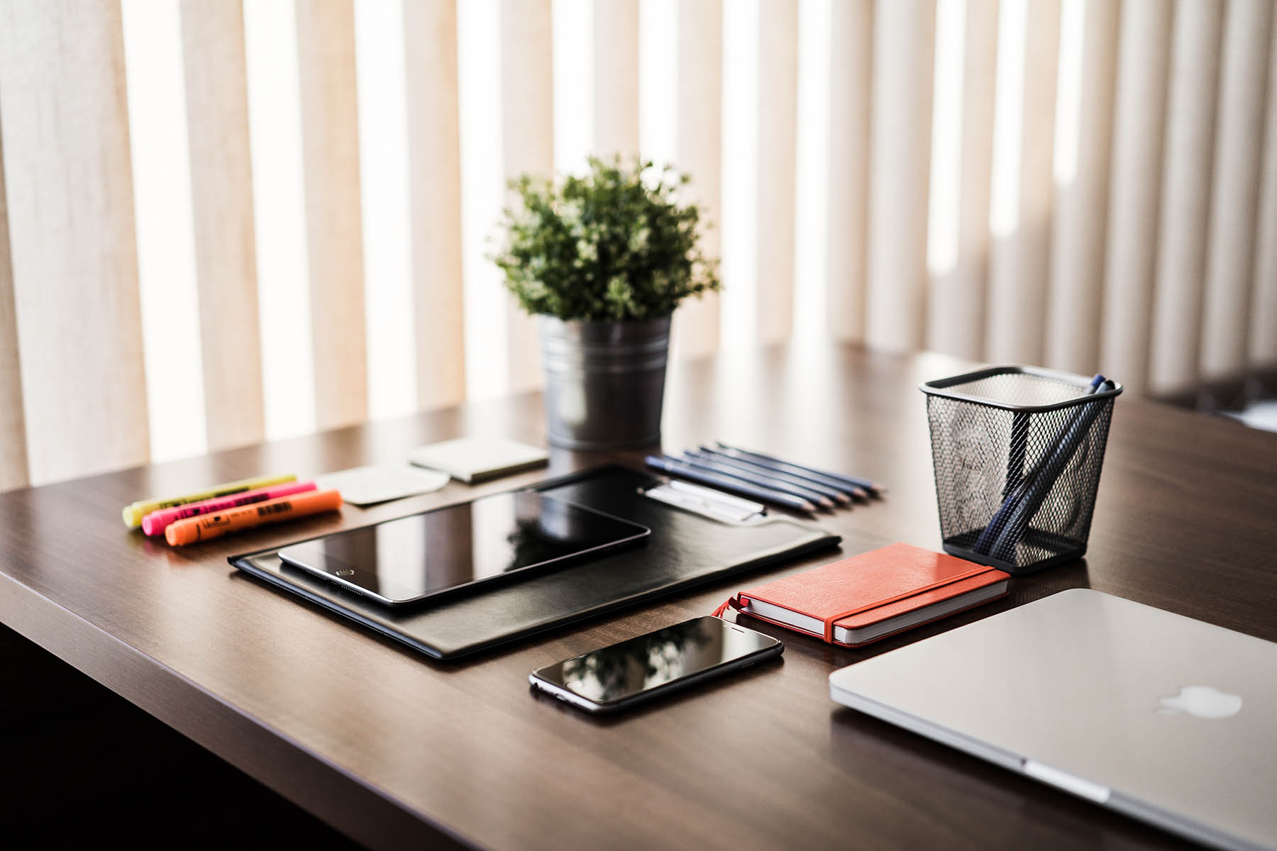 Tidy desk with laptop, tablet, smartphone, note pad and various pens